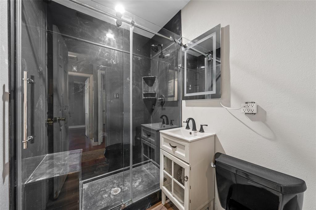 2225 Mitchell Avenue Waco, TX 76708 - Photo 10 of 16 Bathroom featuring a glass-enclosed shower with black-toned wall panels, a white vanity with integrated sink, a black toilet, and an illuminated medicine cabinet