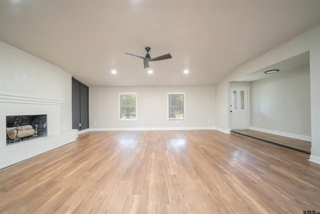 an empty room with wooden floor fireplace and windows