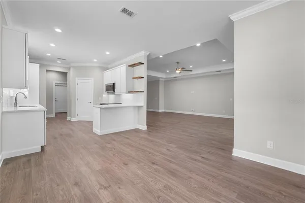 a large kitchen with stainless steel appliances a sink dishwasher a refrigerator and white cabinets with wooden floor