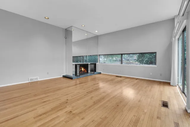 an empty room with wooden floor fire place and windows