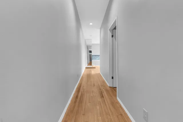 a view of a hallway with wooden floor and a bathroom