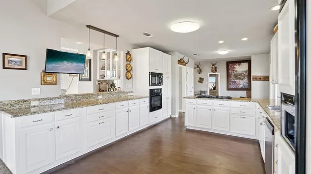 a large white kitchen with granite countertop a large counter top appliances and cabinets