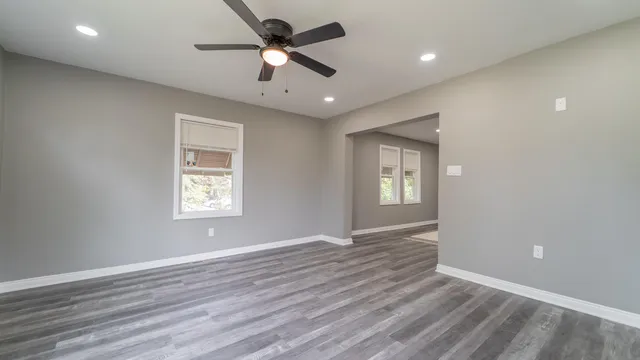 an empty room with wooden floor ceiling fan and windows