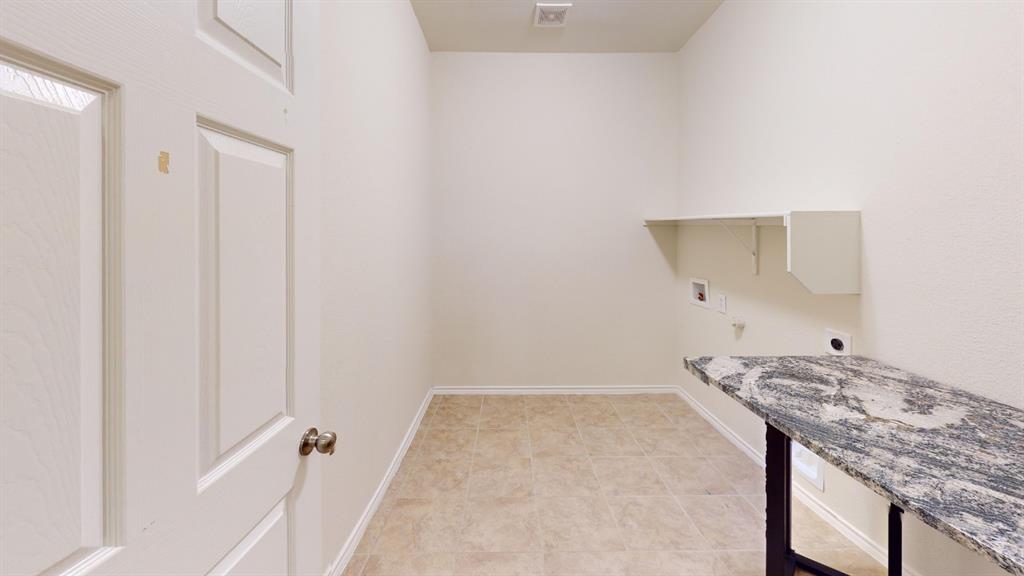 2213 Heaton Street Forney, TX 75126 - Photo 12 of 14 Utility room featuring neutral-toned tile flooring, light wall paint, a built-in wall shelf, and a freestanding granite-finish countertop