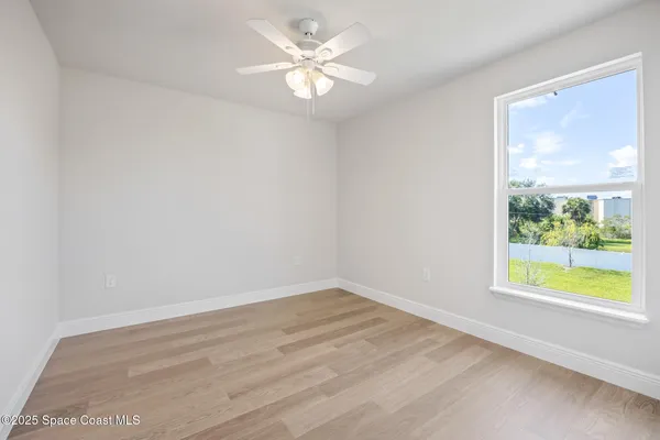 a view of an empty room with window and chandelier fan