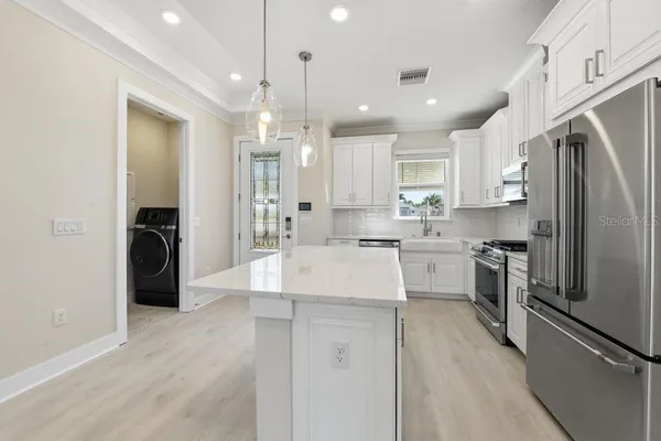 a kitchen with stainless steel appliances granite countertop a refrigerator a sink dishwasher a stove and white cabinets with wooden floor