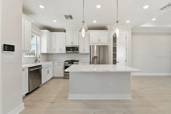 a large kitchen with stainless steel appliances kitchen island granite countertop a stove a sink a refrigerator and white cabinets with wooden floor