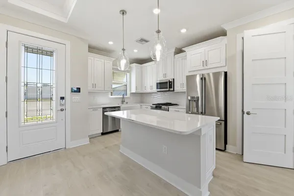 a large white kitchen with a refrigerator a stove a sink dishwasher a oven with white cabinets and wooden floor