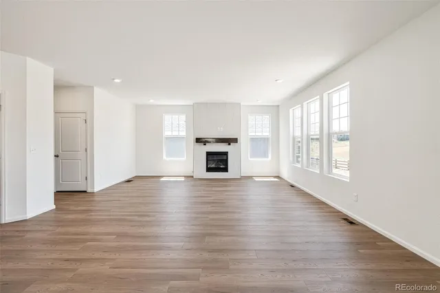 an empty room with wooden floor fireplace and windows