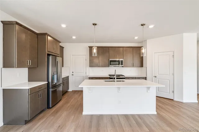 a kitchen with stainless steel appliances a stove a sink a refrigerator and white cabinets with wooden floor