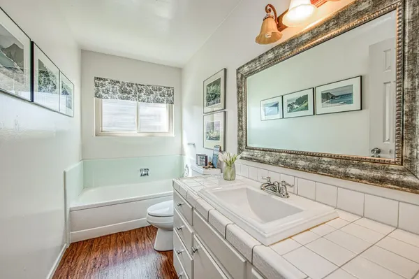a bathroom with a granite countertop sink a toilet a mirror a bathtub and shower