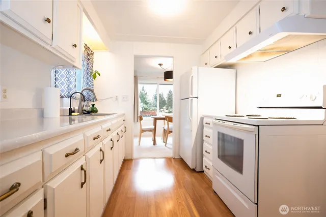 a kitchen with granite countertop a white stove refrigerator and white cabinets with wooden floor