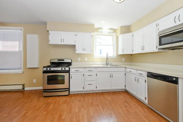 a kitchen with a stove white cabinetry and wooden floor