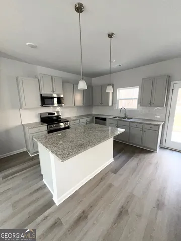 a large kitchen with stainless steel appliances granite countertop a stove a sink dishwasher a refrigerator and a wooden floor