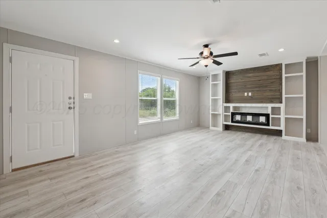 an empty room with wooden floor ceiling fan and windows