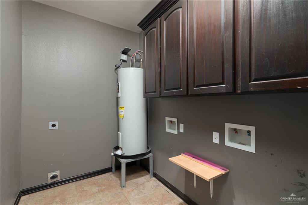 401 Ric Mar Street Edinburg, TX 78541 - Photo 15 of 18 Laundry area featuring dark wood cabinetry, a water heater, and a wall-mounted folding shelf