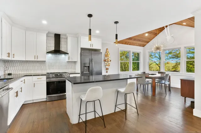 a kitchen with stainless steel appliances granite countertop a stove top oven a sink a dining table and chairs with wooden floor