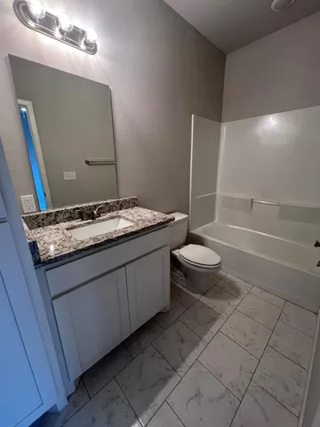 a bathroom with a granite countertop sink a toilet a mirror and bathtub