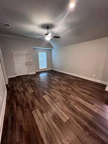 an empty room with wooden floor a ceiling fan and windows