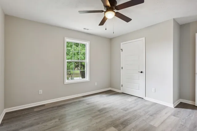 an empty room with wooden floor fan and windows