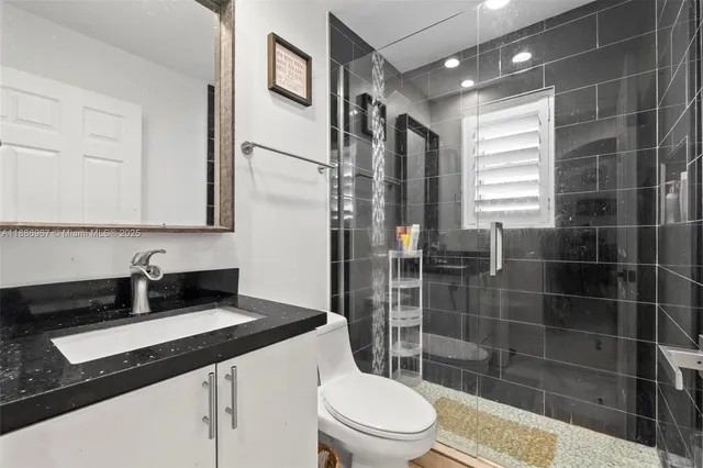 a bathroom with a granite countertop sink a toilet a mirror and shower