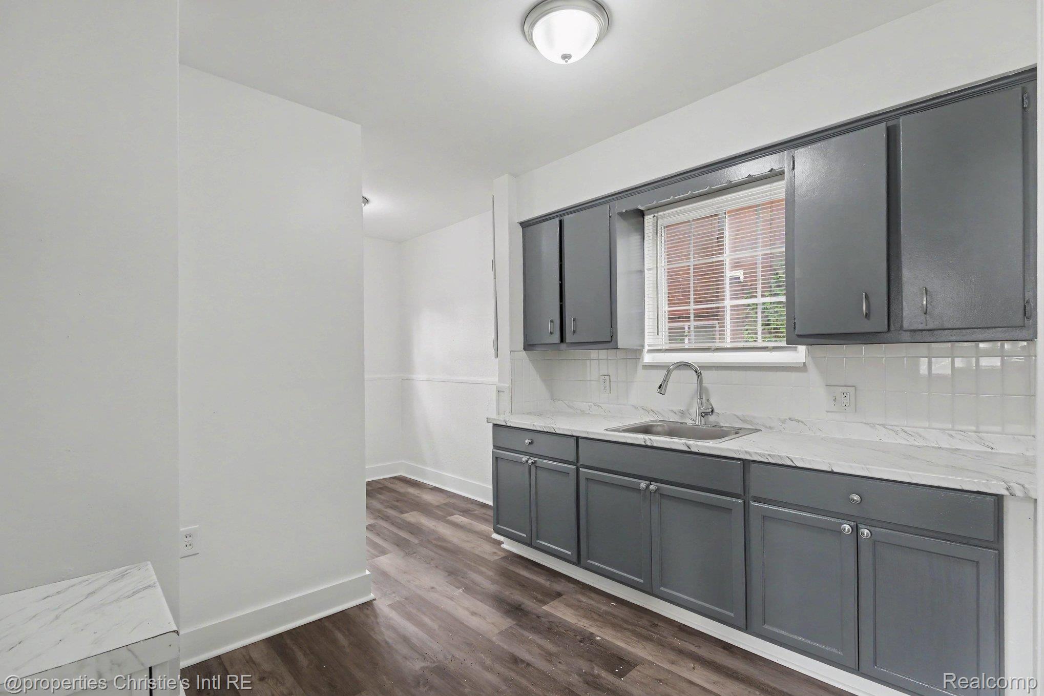 5911 Yorkshire Road Detroit, MI 48224 - Photo 7 of 14 Modern kitchen featuring gray cabinetry, white countertops, a stainless steel sink with a gooseneck faucet, a white subway tile backsplash, and wood-finish flooring