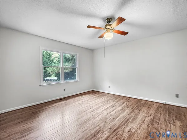 an empty room with wooden floor fan and windows