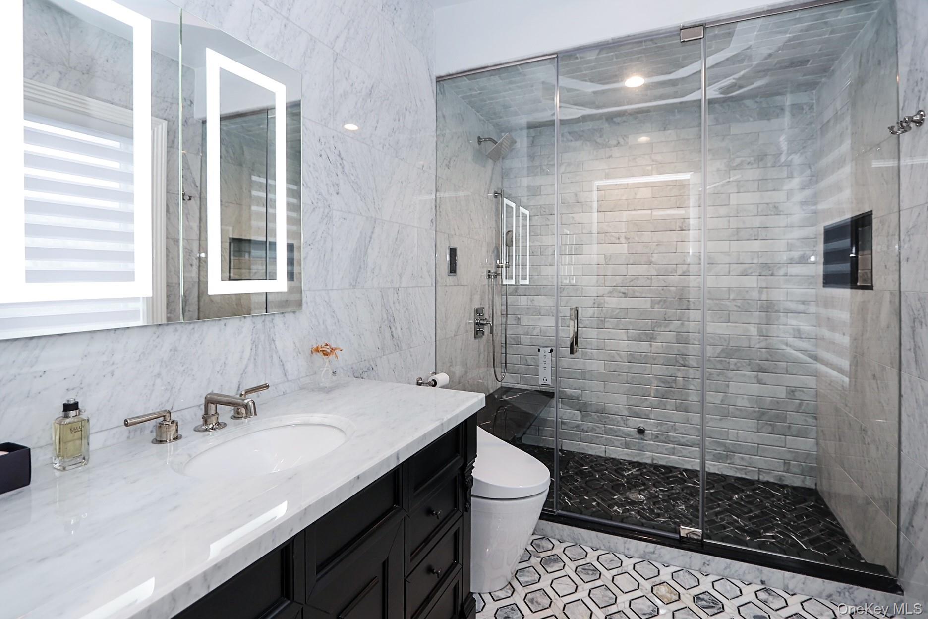 19 Gilbert Road Great Neck, NY 11024 - Photo 26 of 36 a bathroom with a sink a toilet a glass door shower and a mirror