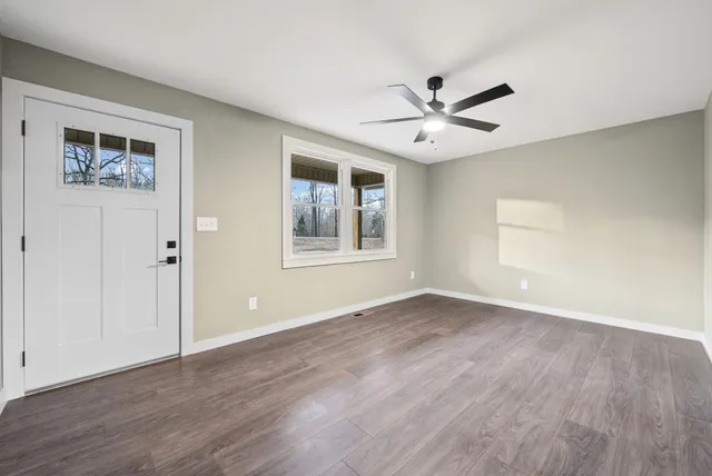 a view of an empty room with wooden floor and a ceiling fan