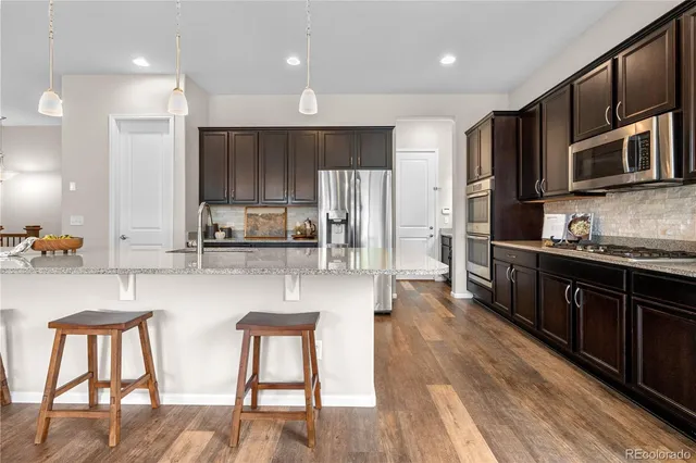 a kitchen with stainless steel appliances granite countertop a refrigerator a stove top oven a sink dishwasher and wooden cabinets with wooden floor