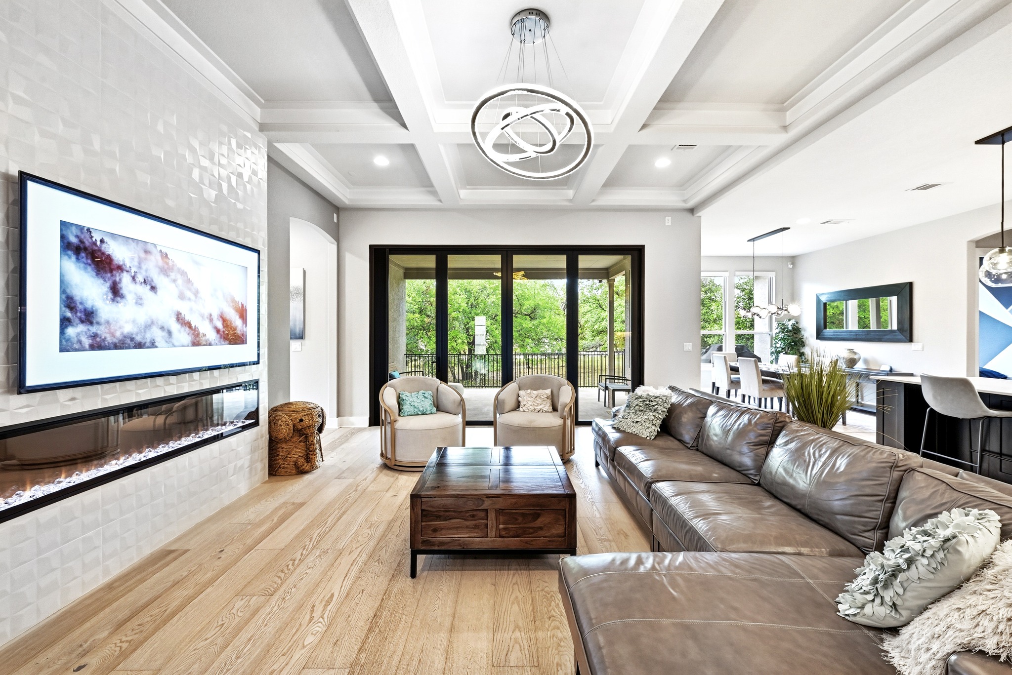 9008 Harper Rae Drive Austin, TX 78717 - Photo 7 of 39 Spacious living area featuring light wood-finish flooring, a contemporary fireplace with a textured white tile surround, coffered ceilings, and a modern chandelier