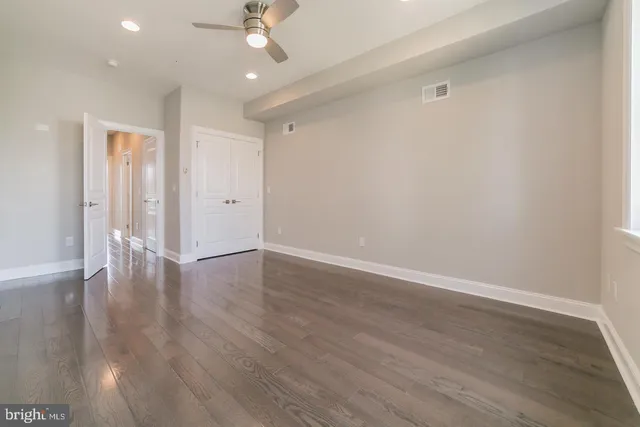 a view of an empty room with wooden floor and a ceiling fan