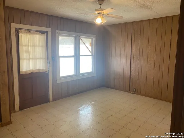 an empty room with chandelier fan and windows