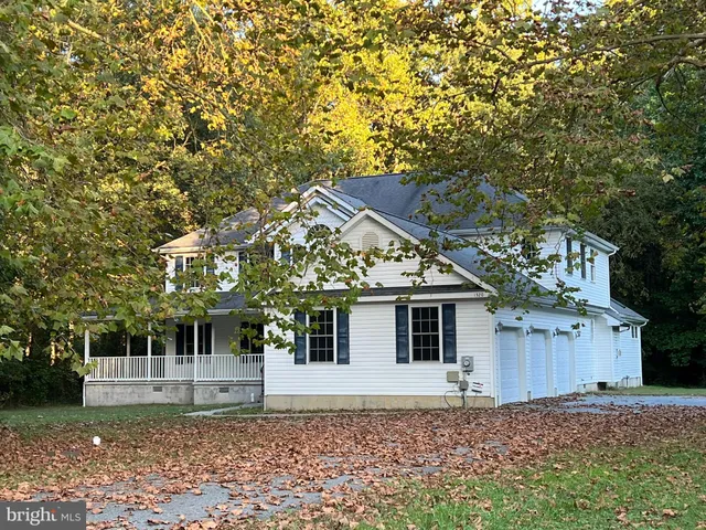 a view of a white house with a large tree and wooden fence