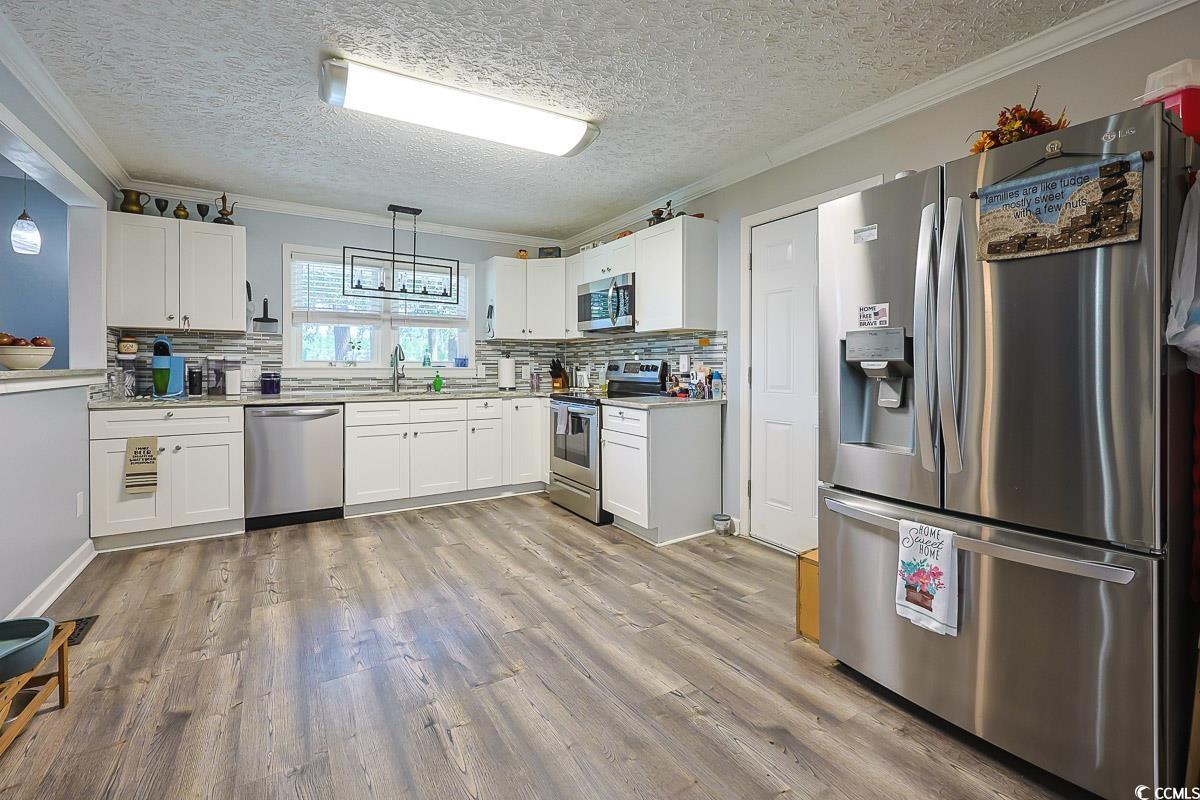 1704 Sherwood Drive Conway, SC 29526 - Photo 3 of 32 Kitchen featuring crown molding, stainless steel appliances, white cabinets, pendant lighting, and light wood-type flooring