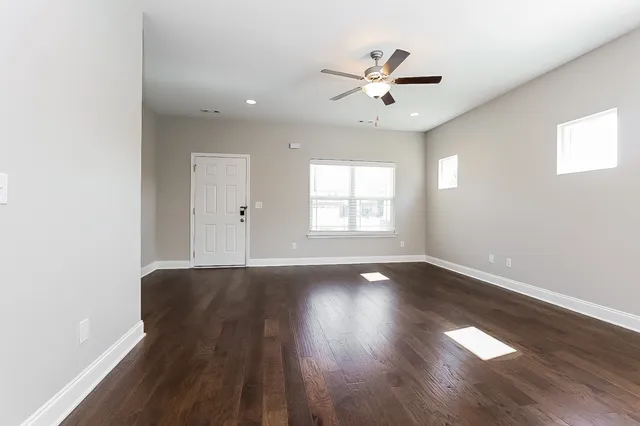 an empty room with wooden floor chandelier fan and windows