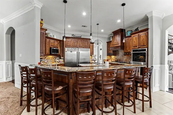 a kitchen with stainless steel appliances kitchen island granite countertop a dining table chairs sink and cabinets
