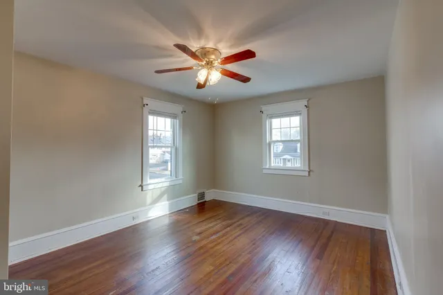 a view of an empty room with chandelier fan and wooden floor
