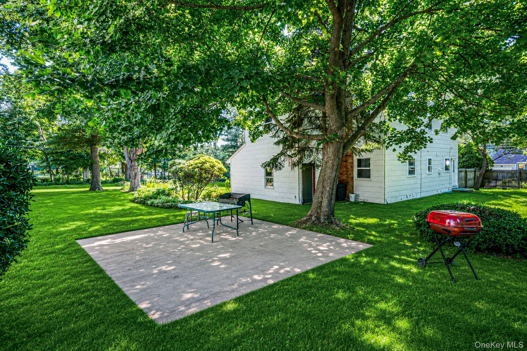 31 Crooked Hill Road Huntington, NY 11743 - Photo 28 of 32 Expansive green lawn with mature shade trees, featuring a square concrete patio and a white exterior home with multiple windows