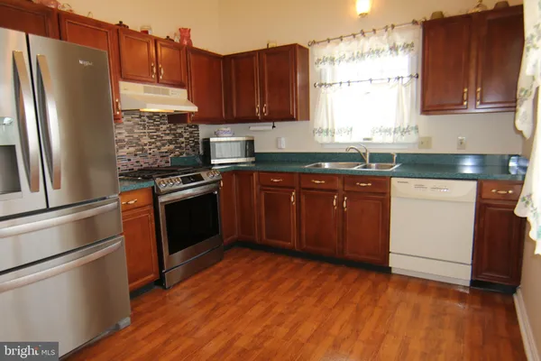 a kitchen with stainless steel appliances granite countertop a refrigerator a sink dishwasher and wooden cabinets with wooden floor