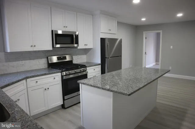 a kitchen with stainless steel appliances granite countertop a sink a refrigerator a microwave a stove and white cabinets