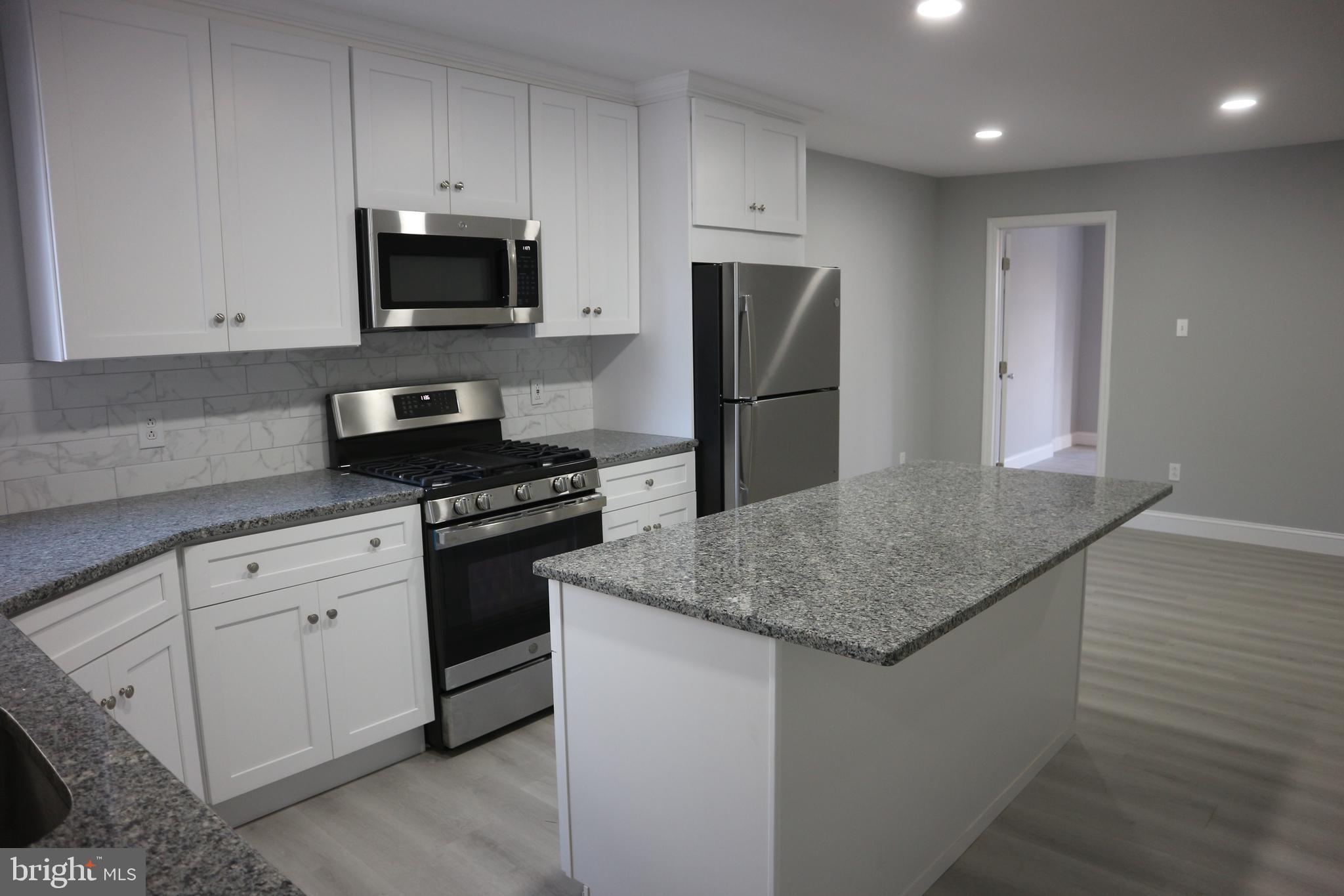 a kitchen with stainless steel appliances granite countertop a sink a refrigerator a microwave a stove and white cabinets