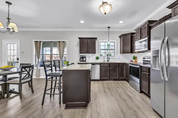 a kitchen with stainless steel appliances a refrigerator a stove a sink dishwasher a dining table and chairs with wooden floor