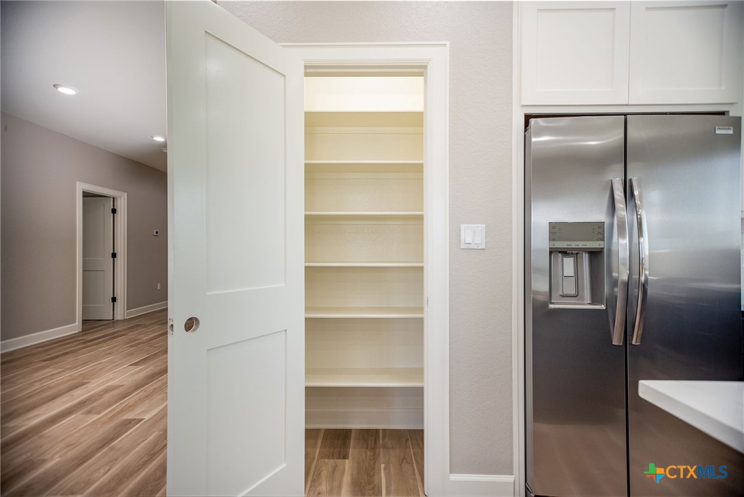 116 Whooping Crane Street Port O'Connor, TX 77982 - Photo 7 of 38 a view of a refrigerator in kitchen and an empty room with wooden floor
