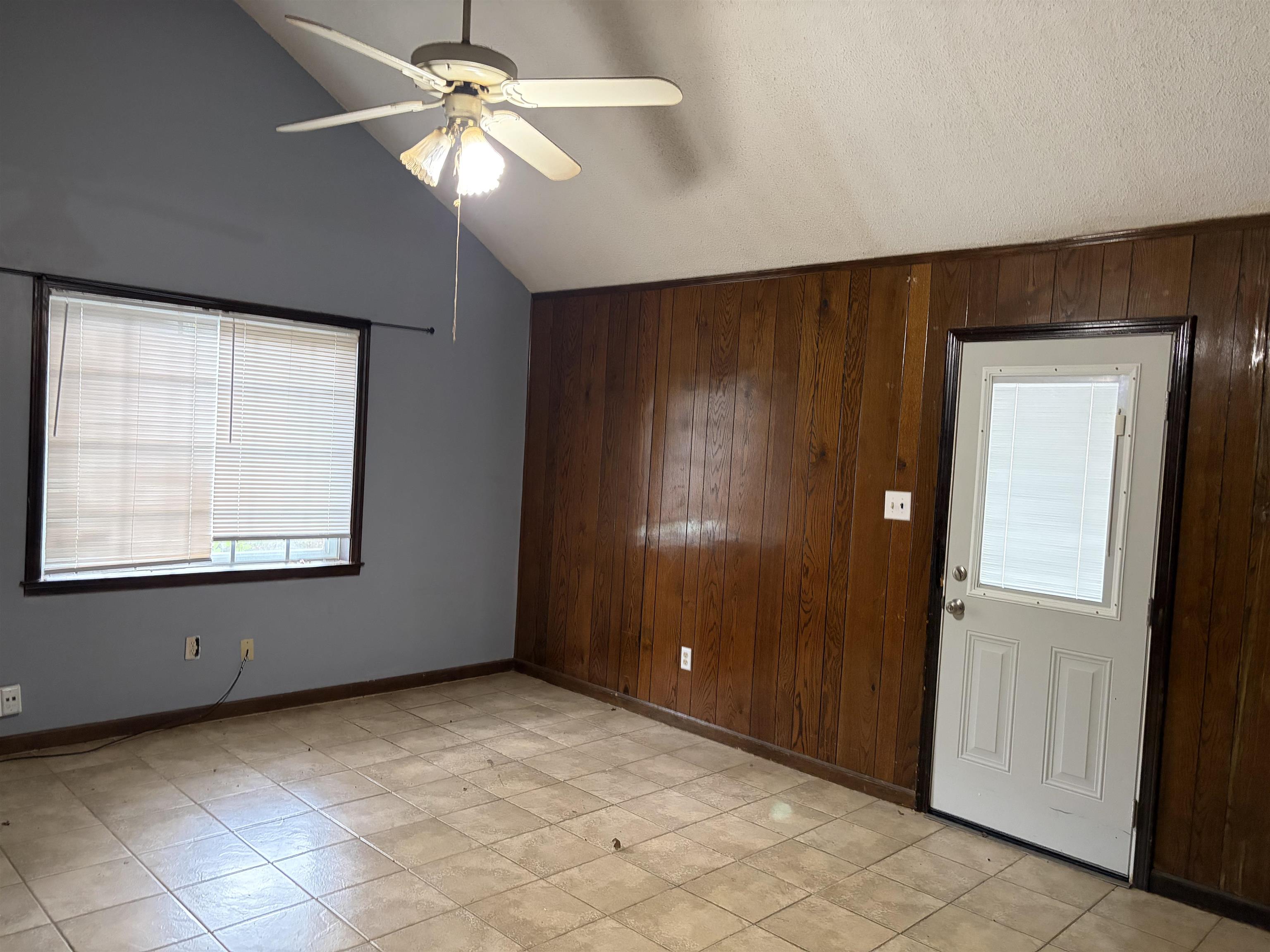 4993 Cedar View Road Memphis, TN 38118 - Photo 7 of 23 Vaulted ceiling with a ceiling fan, light-toned tile flooring, wood paneling, a white door with an integrated window blind, and a window with horizontal blinds