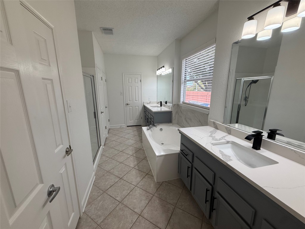 11711 Rydalwater Lane Austin, TX 78754 - Photo 12 of 20 Bathroom featuring two vanities, a bath, a textured ceiling, a shower stall, and light tile patterned floors