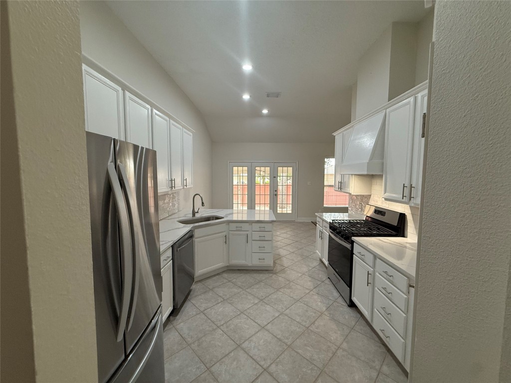 11711 Rydalwater Lane Austin, TX 78754 - Photo 5 of 20 Kitchen featuring a textured wall, a peninsula, stainless steel appliances, white cabinets, and tasteful backsplash