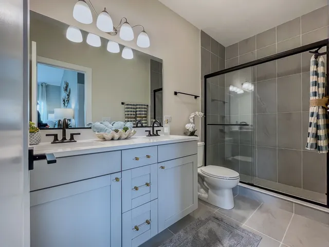 a spacious bathroom with a double vanity sink a toilet a mirror and shower