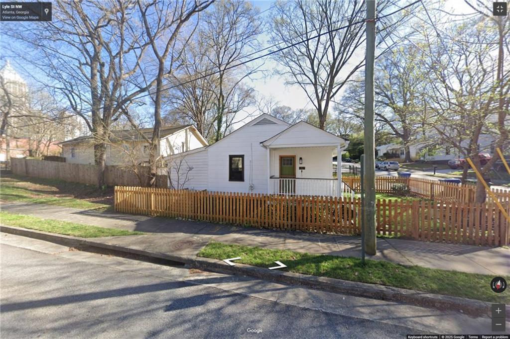 a view of a white house with a small yard and large tree and wooden fence