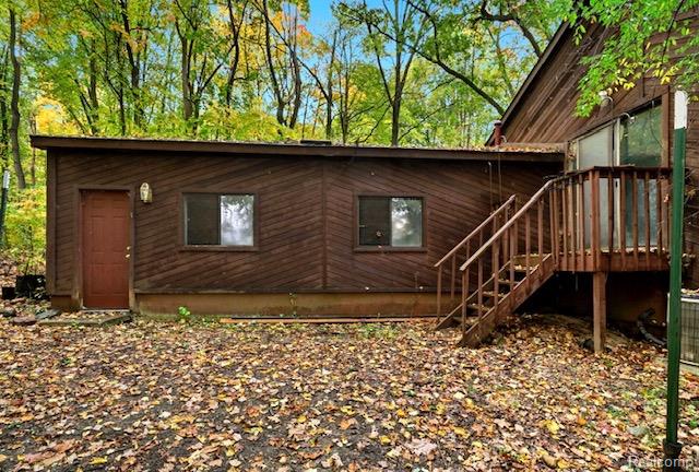 8890 Tipsico Lake Road Holly, MI 48442 - Photo 2 of 20 Wood-paneled exterior featuring a brown entry door, two windows, and an exterior light fixture